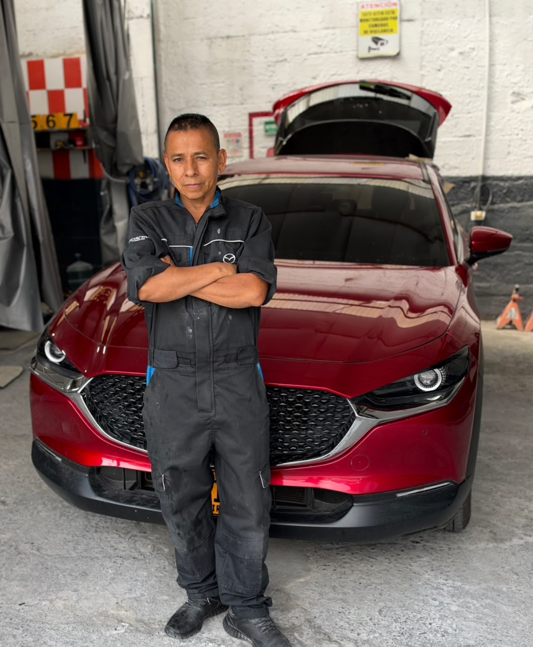 Memo, de brazos cruzados frente a una Mazda roja en su taller