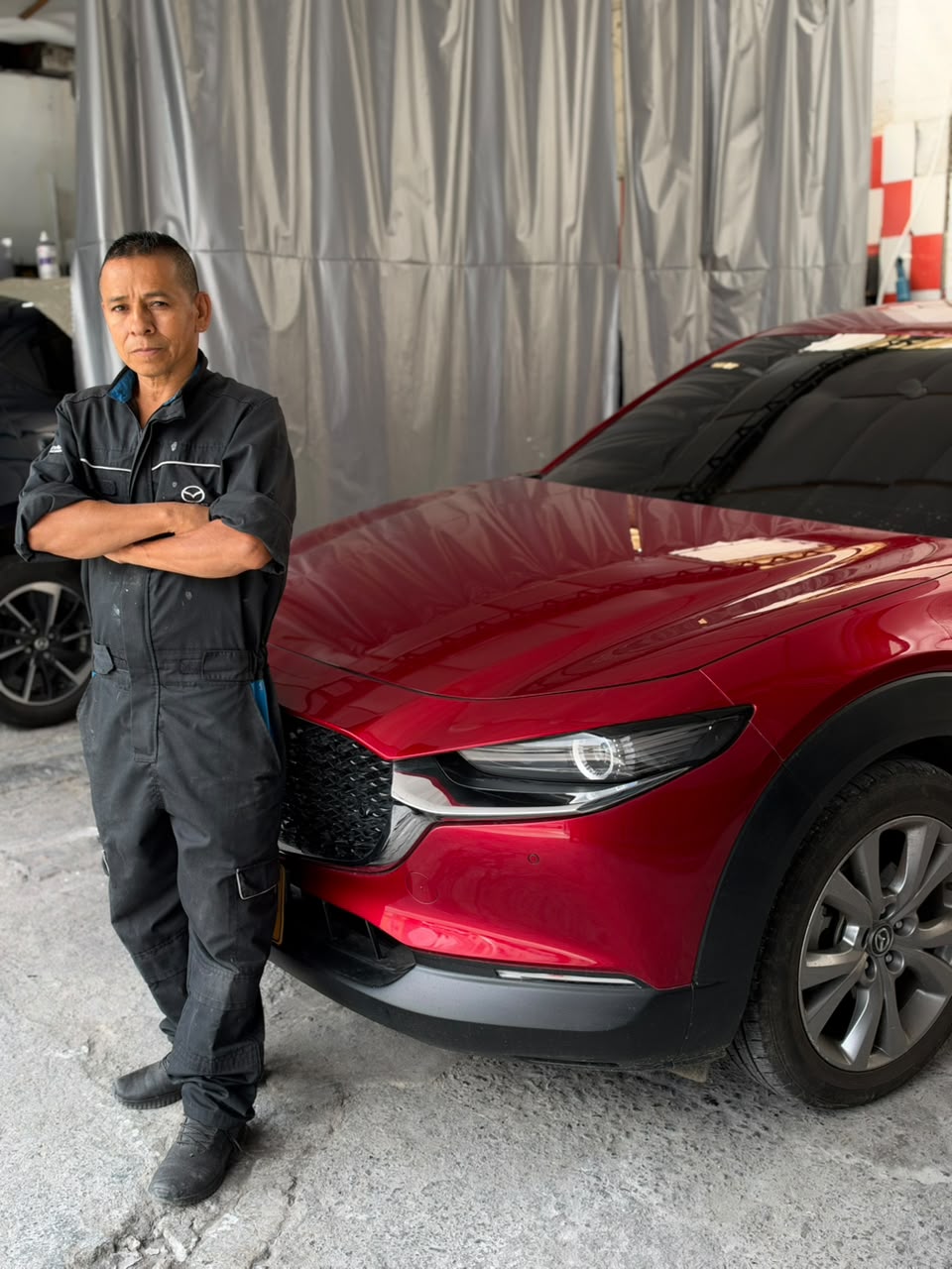 Memo, de brazos cruzados junto a una Mazda roja dentro de su taller